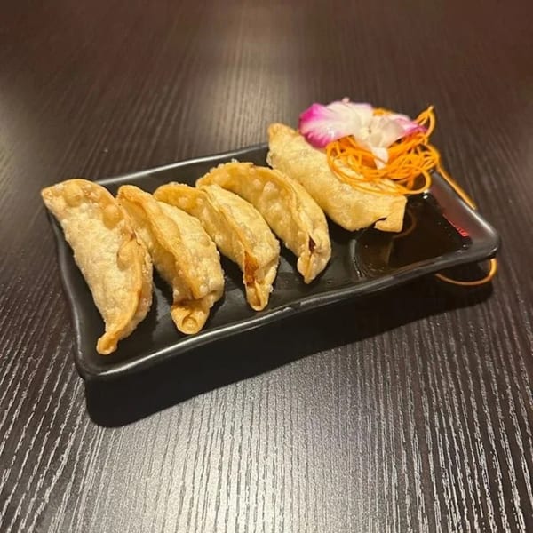 Five golden-brown fried dumplings with a side of sauce, garnished with a flower and shredded carrots.