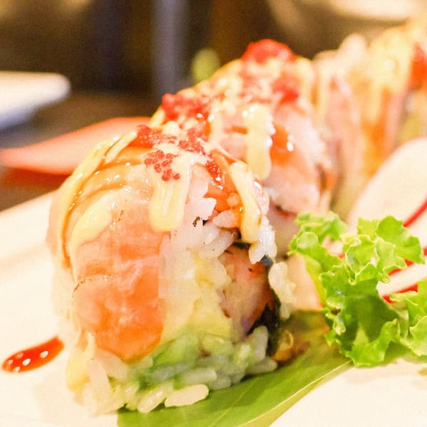 Kanpai Sushi's colorful sushi roll with salmon, avocado, and roe, drizzled with sauce.