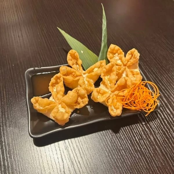 Crispy crab rangoon appetizers with dipping sauce and shredded carrots on a black plate.