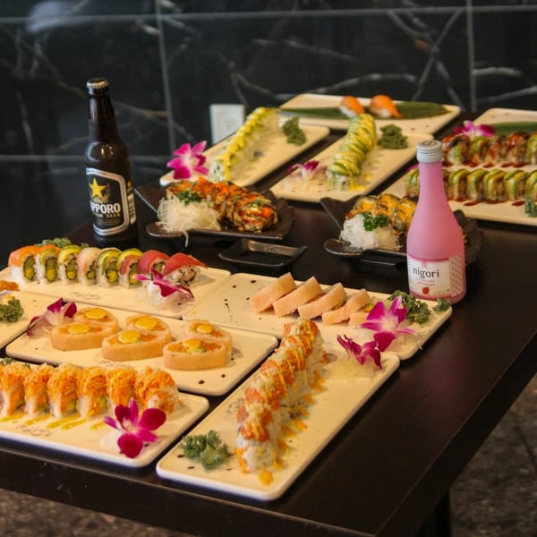 A table laden with various sushi rolls, nigiri, and a bottle of Sapporo beer and pink sake.