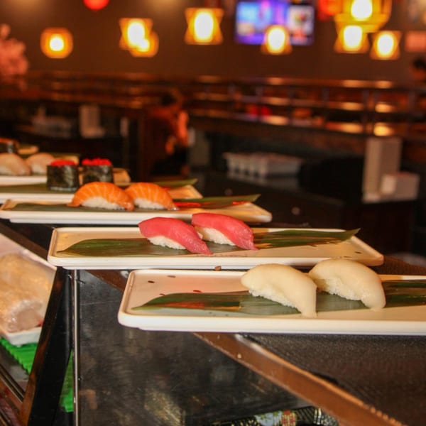 Plates of fresh Kanpai Sushi nigiri and maki rolls displayed on a dark counter in a restaurant.
