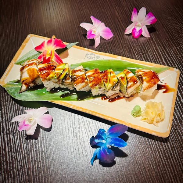 Kanpai Sushi's dragon roll with eel, avocado, and sauce, garnished with orchids, ginger, and wasabi.