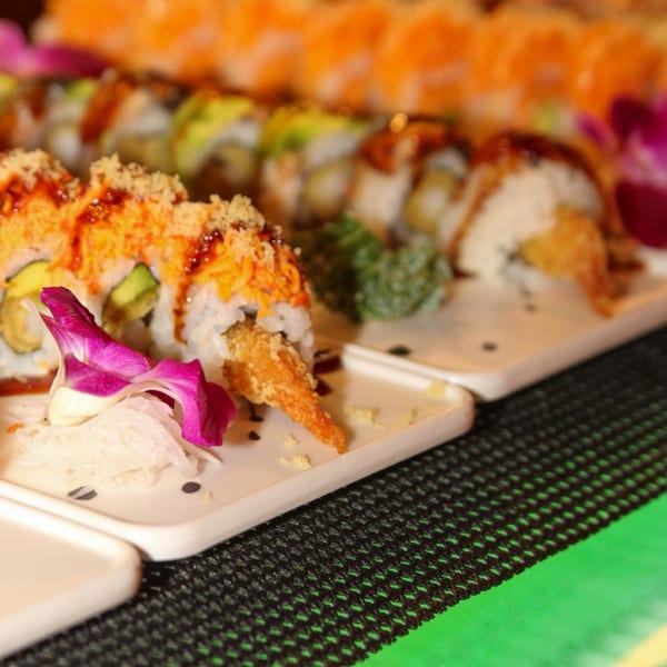 Plates of Kanpai Sushi rolls with avocado, tempura, and a purple orchid garnish.